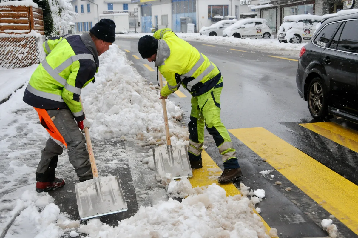 Man sieht zwei Männer Schneeschaufeln.